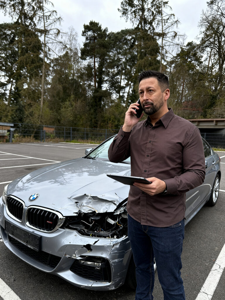 Kfz Sachverstaendiger telefoniert nach einem Verkehrsunfall vor einem beschaedigten Fahrzeug
